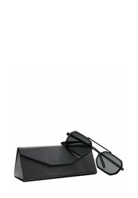 Occhiali da sole neri con montatura ottagonale e lenti oscurate, appoggiati su un astuccio triangolare nero dalla texture strutturata.