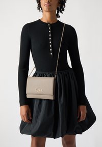 Abito lungo a maniche lunghe nero a coste con dettagli in bottoni e gonna arricciata, abbinato a una borsa a tracolla in pelle taupe con logo dorato.