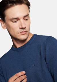 Granatowy sweter z okrągłym dekoltem wykonany z dzianiny, z subtelnym logo na piersi i teksturowanym wykończeniem.