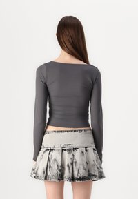 Gray long-sleeve top with a fitted design, paired with a pleated skirt featuring a gray and black tie-dye pattern.