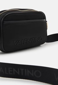Svart Valentino axelremsväska med slät yta, präglad logotyp, guldfärgad dragkedja och justerbar rem med logotryck.