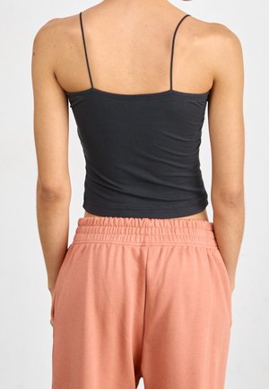 Personne portant un crop top noir à fines bretelles et un pantalon ample couleur pêche avec une ceinture élastique, vue de dos.