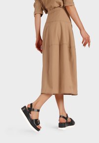 Infradito nere con suola bianca spessa, cinghia alla caviglia e dettaglio con fibbia rotonda, abbinate a una gonna beige a campana lunga fino al ginocchio.