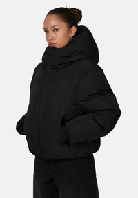 Czarna kurtka puchowa z wysokim kołnierzem i kapturem. Posiada zamek z przodu, elastyczne mankiety oraz boczne kieszenie. Teksturowany materiał, ocieplona konstrukcja.