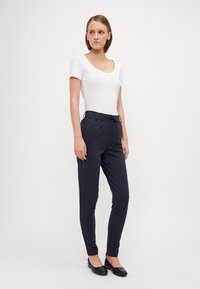 Marine joggebukser med snor i livet, sidelommer og avsmalnet ben-design. Kombinert med en tettsittende hvit t-skjorte med kort erme og svarte leiligheter.