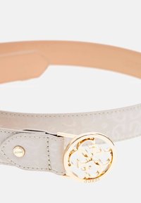 Beige geblokte riem van synthetisch materiaal met een gouden ronde gesp met het "GUESS"-logo. Inclusief een metalen drukknoop voor sluiting.