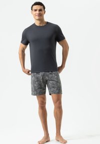 Gray short-sleeve t-shirt paired with patterned navy shorts featuring a paisley design. Model standing barefoot against a plain background.