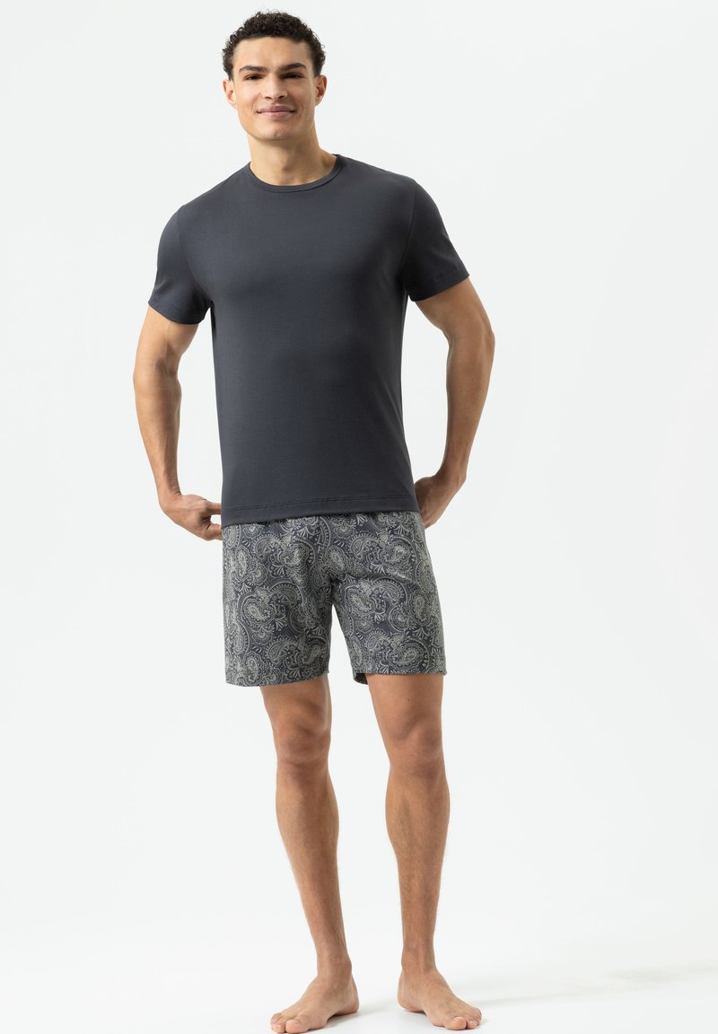 Gray short-sleeve t-shirt paired with patterned navy shorts featuring a paisley design. Model standing barefoot against a plain background.