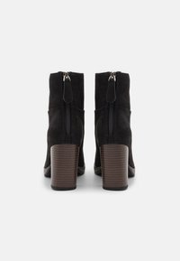 Black suede ankle boots with a straight design, zipper detail at the back, and brown wooden block heels. Smooth texture, durable construction.