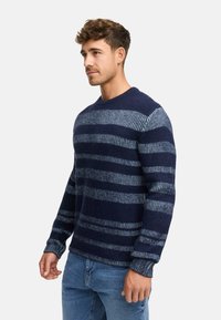 Mørkeblå stribet sweater med varierende nuancer, tekstureret stof, rund hals og ribbede manchetter, parret med denimjeans.