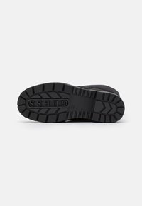 Suela de goma negra con dibujo texturizado, que presenta un prominente logo de 'GUESS'. Material superior lujoso, sin herrajes ni acentos visibles.