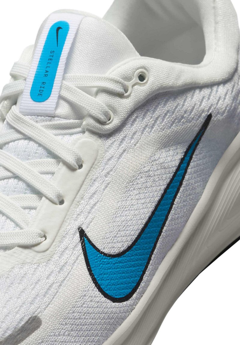Zapatilla deportiva blanca con parte superior texturizada y Swoosh azul de Nike. Presenta cordones ligeros, un cuello acolchado y una etiqueta azul que dice "Stellar Ride".