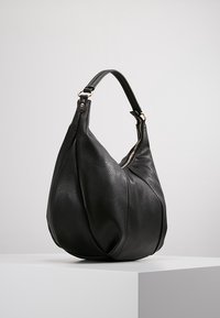 Svart läder axelväska med rundad form, med en texturerad yta och ett gyllene dragkedjeinslag. Slät handtag för bärande.