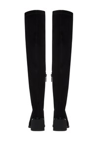 Par de botas negras hasta la rodilla con tacones de bloque, costuras visibles y cremalleras laterales, mostradas desde atrás sobre un fondo blanco.