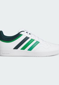 Zapatilla deportiva blanca con tres franjas verde y azul marino, parte superior de cuero texturizado, puntera lisa y suela de goma blanca. Logo de la marca en el lateral.