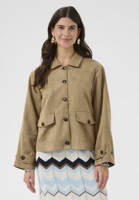 Jachetă din microfibră de culoare maro, cu guler, închidere cu nasturi și două buzunare frontale. Prezintă mâneci largi și nasturi negri.