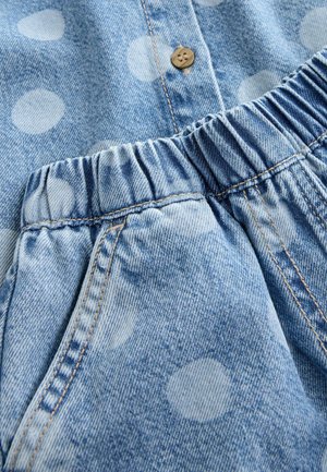 Lyseblåt denimstof med hvide polkaprikker, med en brun knap og elastisk taljebånd. Indeholder synlige sømme og lomme-detalje.