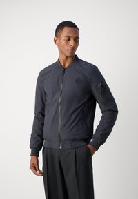 Granatowa bomberka wykonana z lekkiego materiału, z zapięciem na zamek, prążkowanymi mankietami i logo na klatce piersiowej. Slim fit.