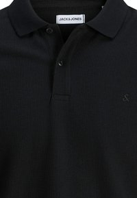 Polo nera con texture, due bottoni, colletto a risvolto e etichetta bianca "JACK & JONES" all'interno dello scollo.