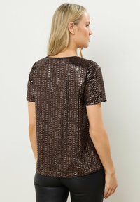 Brun paillet-kortærmet top med lodrette linjer af skinnende pailletter. Blød tekstur og rund halsudskæring. Matched med tætsiddende sorte bukser.
