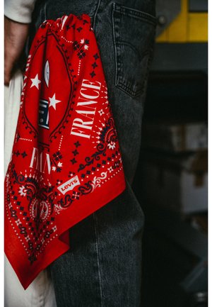 Bandana rouge Levi's avec le texte "FRANCE" et des motifs décoratifs, glissé dans la poche d'un jean en denim foncé.