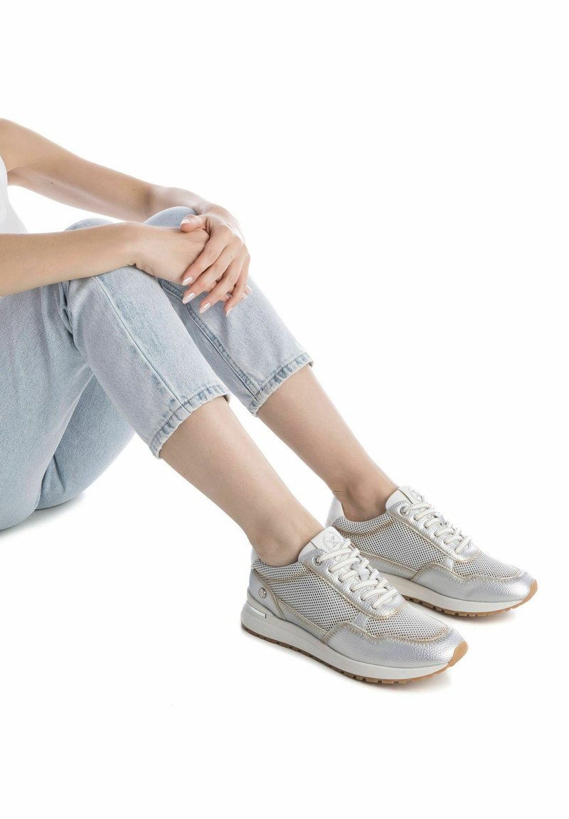 Zapatillas de malla plateadas con un acabado metálico suave, punta redondeada y cordones blancos. Presentan una suela de goma texturizada para mayor tracción.