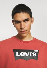 Felpa rossa in cotone con il logo Levi's nero grafico sul petto. Collo rotondo e vestibilità morbida. Tessuto morbido e testurizzato.
