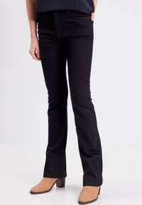 Jeans acampanados negros de denim con una textura suave. Presentan bolsillos en la parte delantera y una cintura ajustada, combinados con botas de tobillo marrón claro.