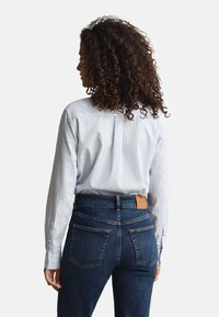 Striped light blue button-up shirt with curved hem, worn with dark blue denim jeans featuring a leather tag and pocket details.