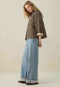 Jasje met luipaardprint en driekwartmouwen, beige mouwen, gecombineerd met lichte blauwe wijde jeans en bruine platte schoenen.