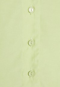 Tecido de camisa verde claro com uma textura suave, apresentando quatro botões iguais alinhados verticalmente ao longo da pala.