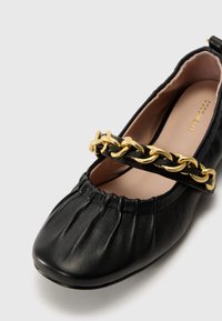 Black leather flat shoe with gathered texture, featuring a gold chain accent across the front strap and a rounded toe design.