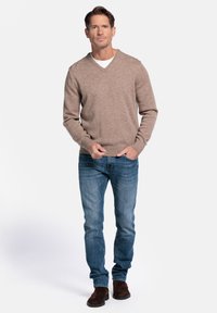 Brauner Pullover mit V-Ausschnitt aus Wollmischung, kombiniert mit blauen Jeans und dunkelbraunen Wildlederstiefeln, der ein lässiges, aber strukturiertes Outfit zeigt.