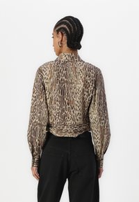 Halenka s leopardím potiskem, s dlouhým rukávem a vysokým límcem, s úzkým pasem a texturovanou tkaninou, spárována s černými kalhotami s vysokým pasem.