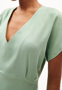 Zielona sukienka w kształcie v z krótkimi rękawami, wykonana z lekkiego materiału. Charakteryzuje się gładką fakturą i dopasowanym krojem.