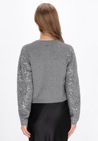 Suéter gris corto con cuerpo texturizado y mangas largas con lentejuelas. Presenta un escote redondo y puños acanalados.