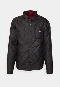 Veste noire matelassée à boutons, deux poches poitrine, doublure intérieure écossaise rouge et logo The North Face sur la poche gauche.