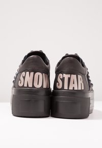 Baskets plateforme noires avec « SNOW » sur le talon gauche et « STAR » sur le talon droit en grandes lettres beiges sur un fond uni.