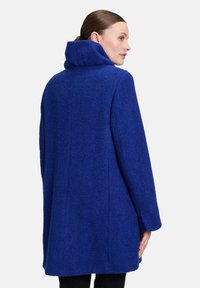 Manteau en laine bleu texturé avec un grand col et des manches longues, présente une coupe droite et des coutures discrètes à l'arrière.