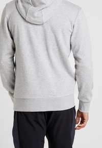 Sudadera gris de tela suave, con capucha ajustable, puños y dobladillo acanalados, de textura lisa y diseño casual.