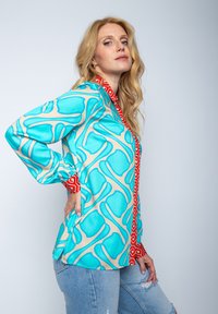 Kolorowa koszula z długim rękawem w abstrakcyjny wzór w kolorach turkusowym i beżowym, z czerwoną kołnierzykiem i listwą guzikową. Gładka tekstura.