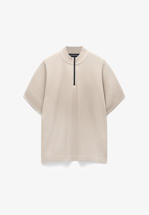 Beige Kurzarmoberteil mit teilweisem Reißverschluss und hohem Kragen; mit vertikal gerippter Textur. Leichter Stoff mit lockerem Sitz.