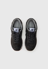 Black suede sneakers with mesh accents; padded collar, dark gray laces, and logo on tongue; rubber sole with brown tread pattern.
