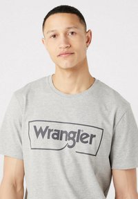 Grey short-sleeve t-shirt made from cotton, featuring a large black "Wrangler" logo in a rounded rectangle across the chest.
