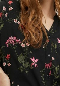 Sort skjorte med blomsterprint med pink og grønne motiver, korte ærmer og knappestolpe foran. Glat stofstruktur.