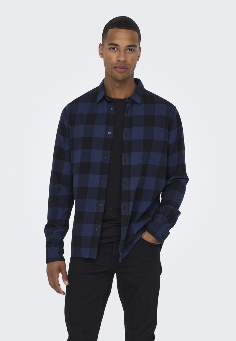 Geruit flanellen shirt in donkerblauw en zwart, met een knoopsluiting aan de voorkant, lange mouwen en een relaxte pasvorm. Zwarte basislaag eronder.