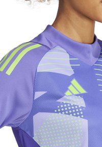 Paarse sportshirt met groene accenten, met geometrische patronen en textuurstof. Inclusief een staande kraag en opvallende strepen op de schouder.