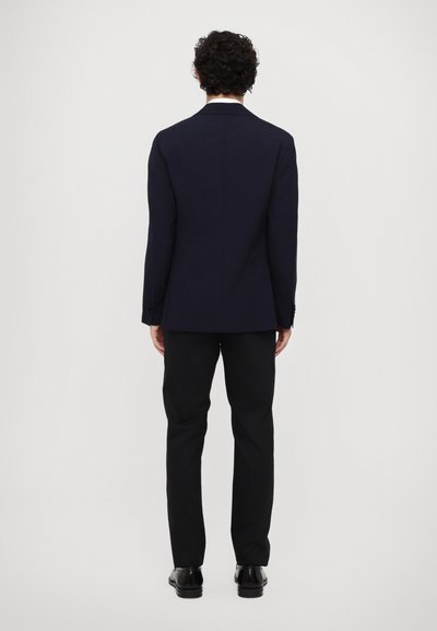 Giacca da abito blu navy con vestibilità su misura, spacco singolo e pantaloni neri eleganti. Tessuto liscio, minimalismo nei dettagli e design classico.