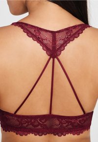 Burgunderfarbener Spitzen-Bralette mit gewellten Kanten, ausgestattet mit einem geflochtenen Rückendesign und floralen Mustern in transparenter Textur.