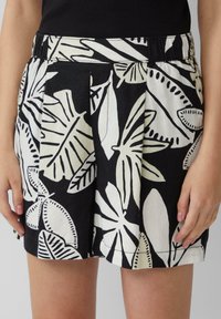 Shorts noirs et blancs avec un motif floral, dotés de plis, fabriqués en tissu léger, avec une ceinture élastique pour plus de confort.
